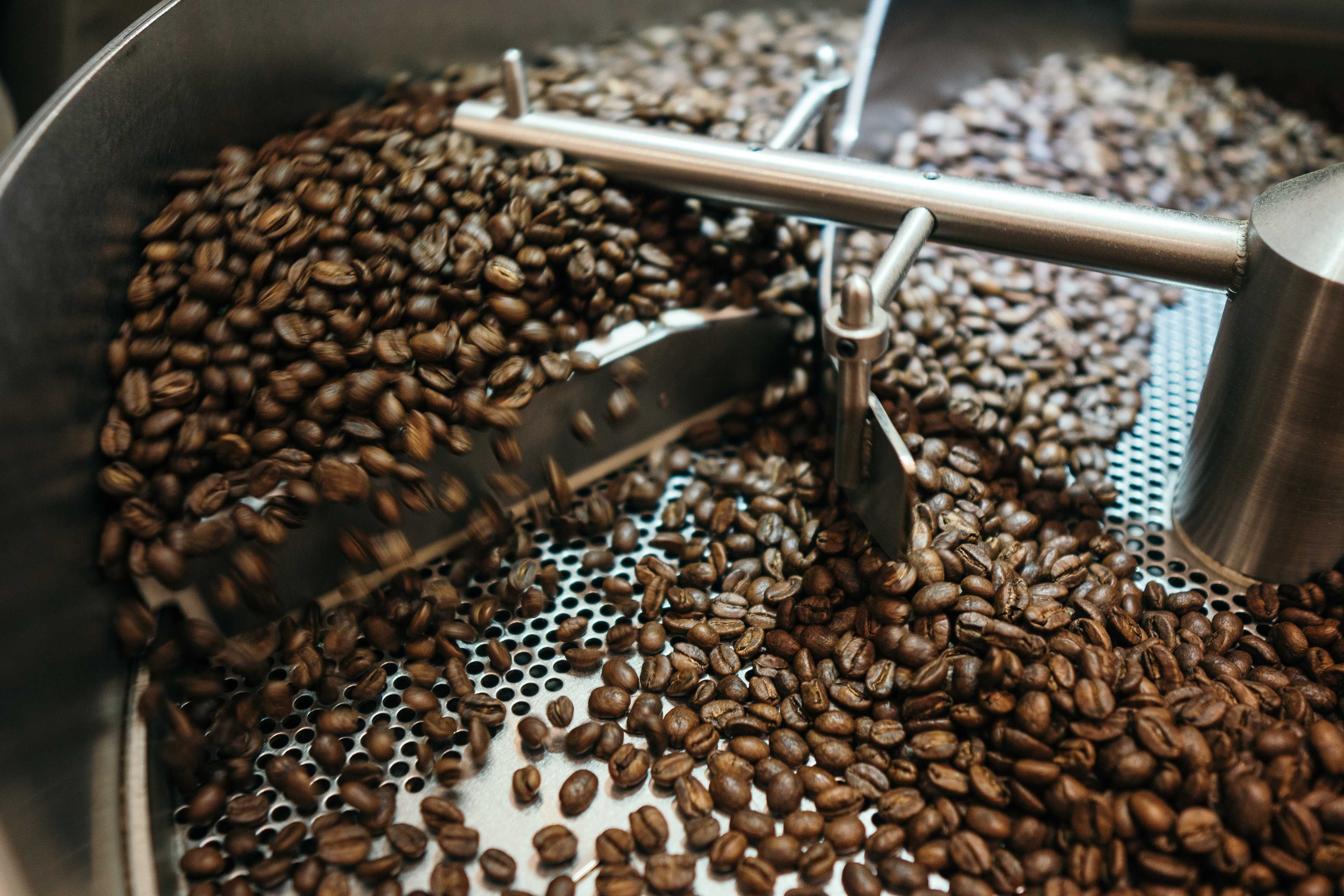 Frisch geröstete Kaffeebohnen im Rösttrommel bei der Verarbeitung, hervorhebend die Qualität des Edel Bitter Espresso.