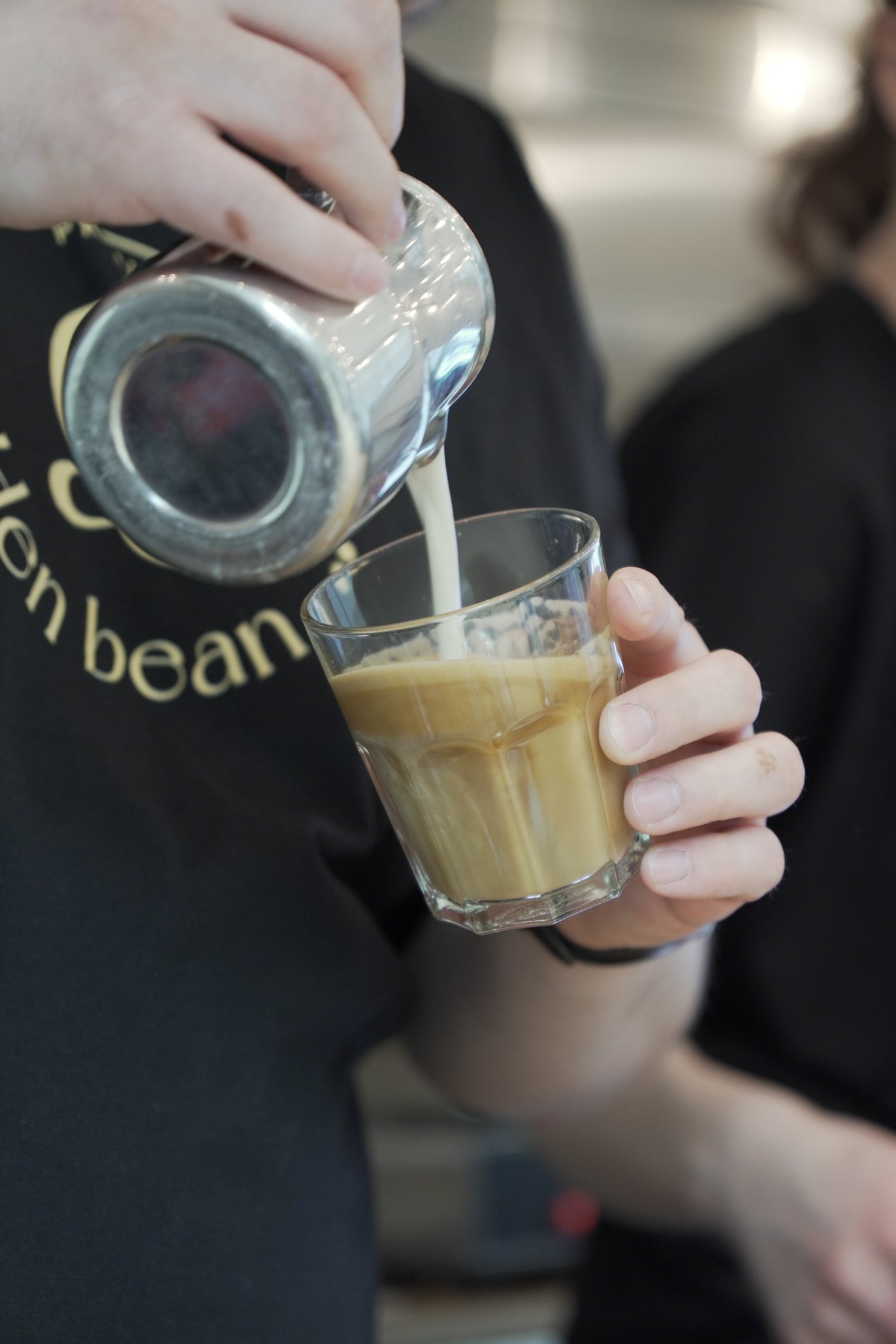 Barista von Golden Bean gießt Milchschaum in einen Kaffee.